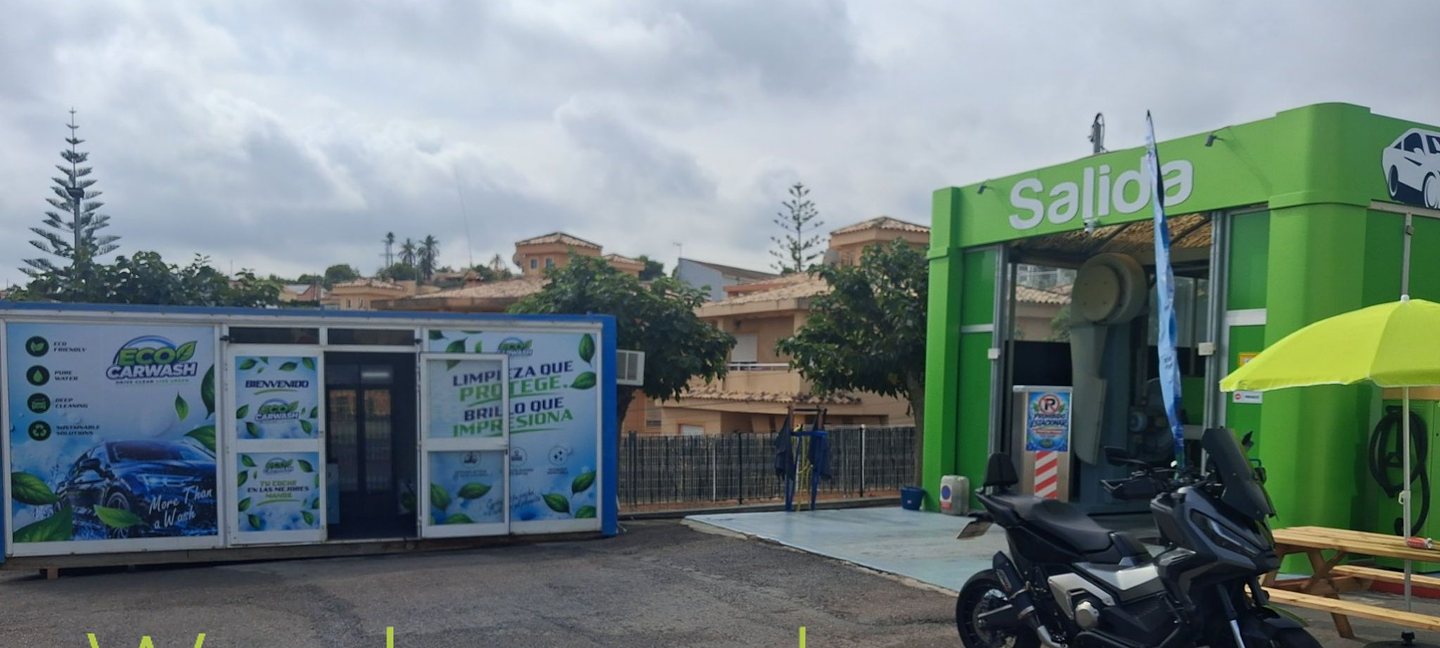 Explanada de Eco Carwash con la oficina, la salida del túnel de lavado y una moto aparcada